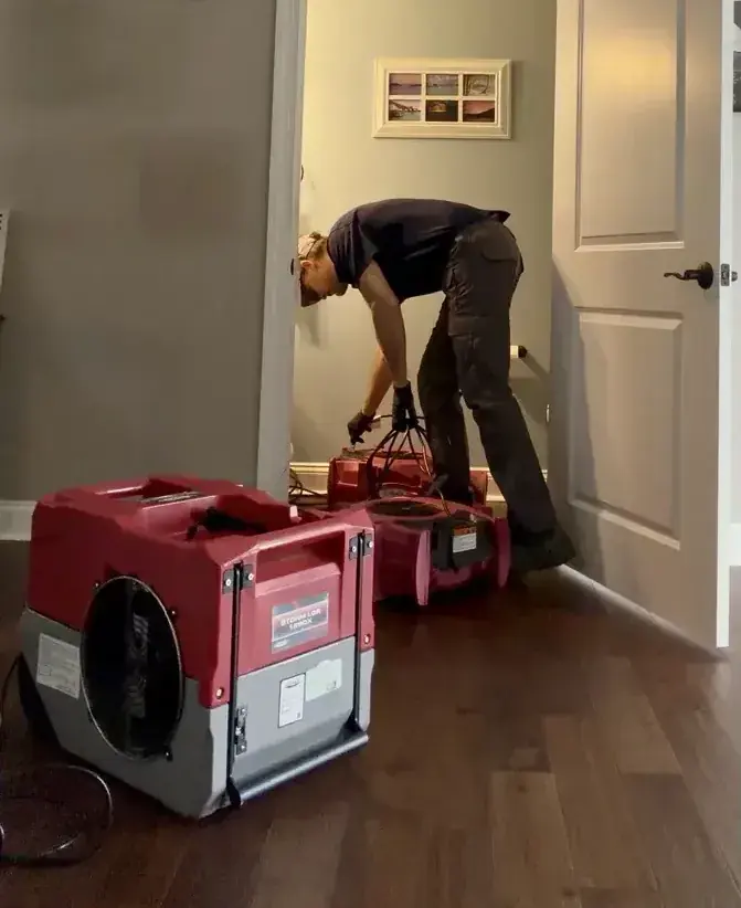 Technician placing an LGR dehumidifier and air movers along a hallway