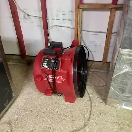 Red air mover beside an opened lower wall with plastic sheeting hung